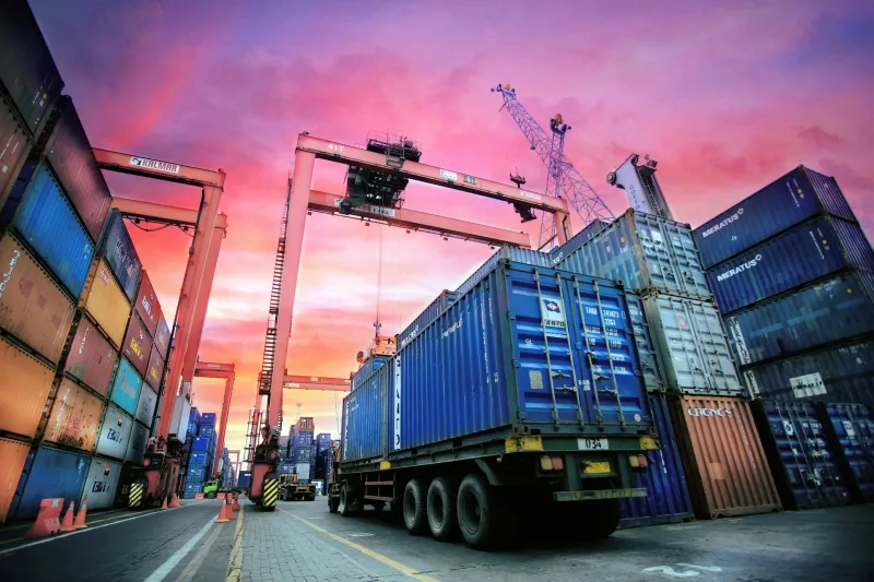 Gestapelte Seecontainer im Hafen vor violettem Abendhimmel